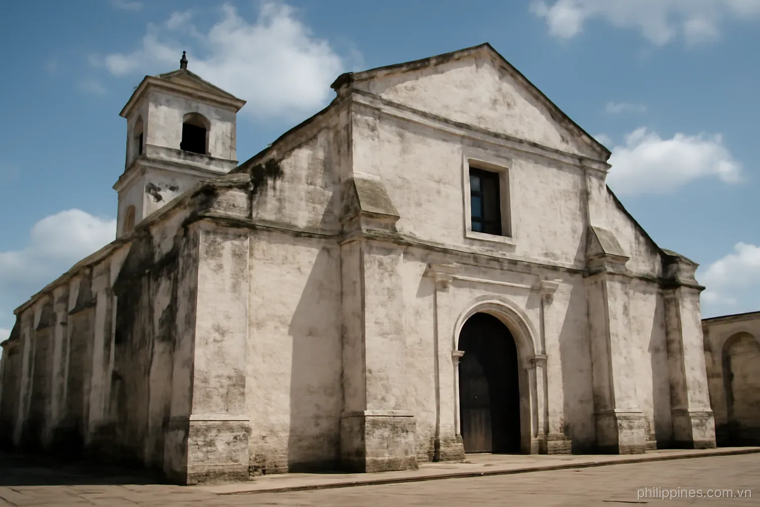 A whitewashed colonial-era stone church facade with heavy buttresses under a bright sky, no readable text